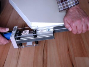 Die überstehende Kante wird entfernt. Eine Hand umfasst den Druckluftmotor, die andere Hand fixiert das vordere Ende an der Kante und in der Mitte der Plattendicke.